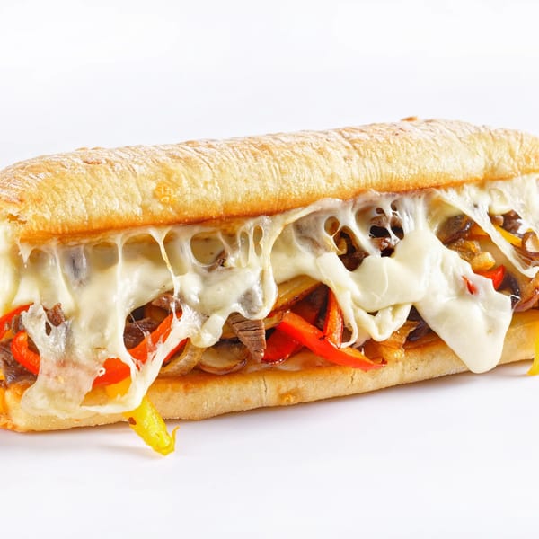 A cheesy steak and pepper sub sandwich with melted mozzarella, red and yellow peppers, and onions.