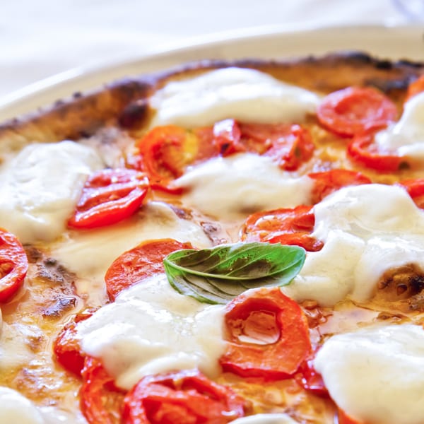 Close-up of a Fabio's Pizza Margherita, with melted mozzarella, red tomatoes, and a fresh basil leaf.