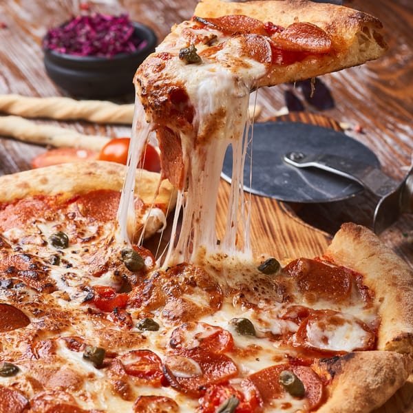 A slice of Fabio's pepperoni pizza with melted cheese stretching, lifted from the whole pizza.